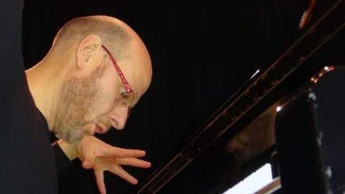 Ein Mann mit Glatze spielt Klavier und singt in ein Mikrofon