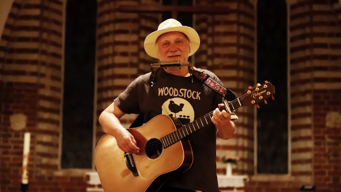 Ein Mann in einem Kirchenschiff spielt Gitarre und trägt einen Strohhut.