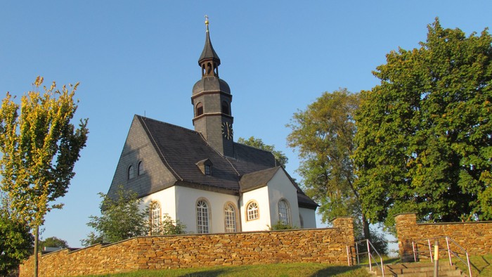 Kleine Kirche mit hohem Turm auf grünem Hügel