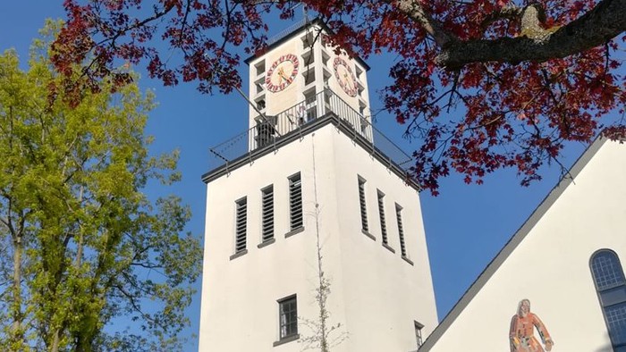 Weißer Turm mit Uhr und Statue unter rotem Baum