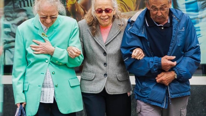 Drei ältere Menschen stehen vor einem Laden und schauen auf ihre Handys