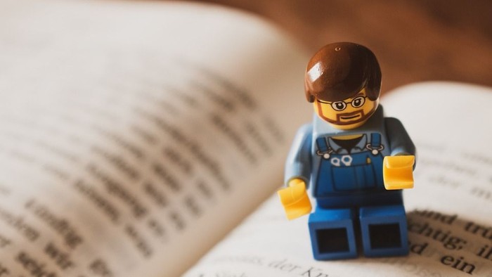 Ein Lego-Männchen sitzt auf einem aufgeschlagenen Buch mit deutschem Text.