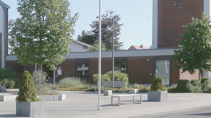 Ein modernes Gebäude mit großen Fenstern und einem gepflegten Außenbereich mit Bäumen und Bänken.