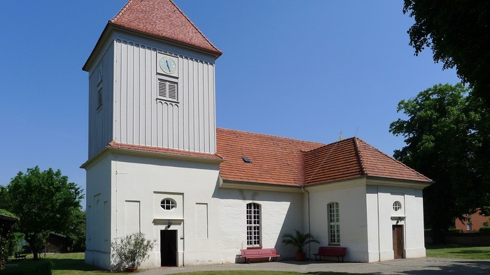 Weißes Kirchengebäude mit hohem Turm und roter Dachziegeln unter blauem Himmel