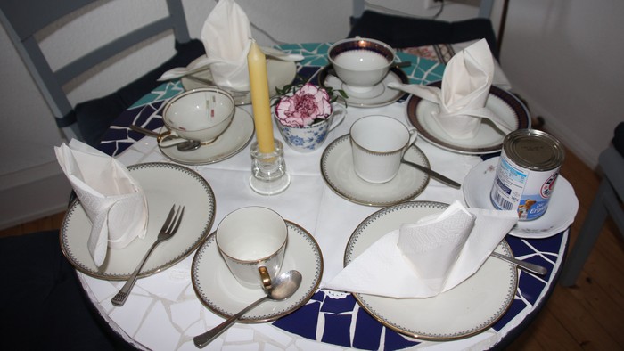 Elegant gedeckter runder Tisch mit Vintage-Porzellan, Servietten und einem Blumenarrangement als Mittelpunkt für eine formelle Teegesellschaft.