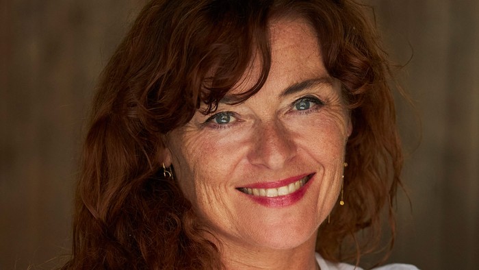 En kvinde med rødt hår og blå øjne, smiler og har et hvide t-shirt på.