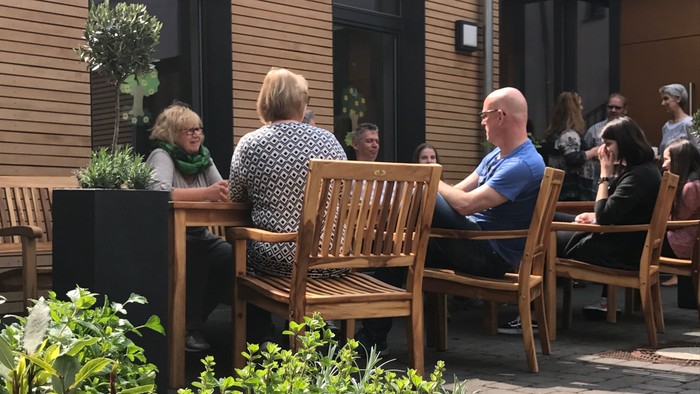 Menschen sitzen auf Holzbänken im Innenhof des Gemeindezentrums Wittenbergstraße