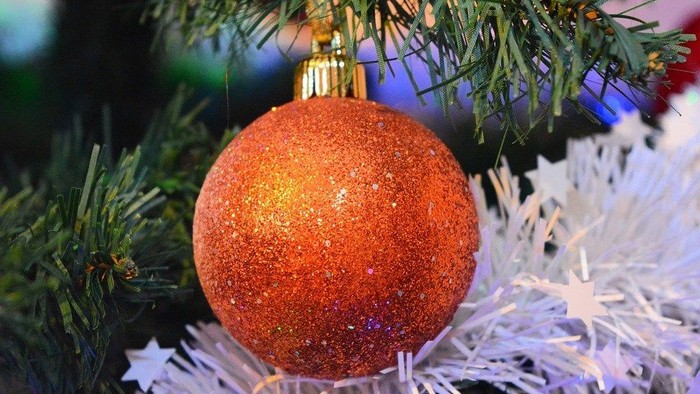 Et orange glitrende pynt med guldtop på juletree