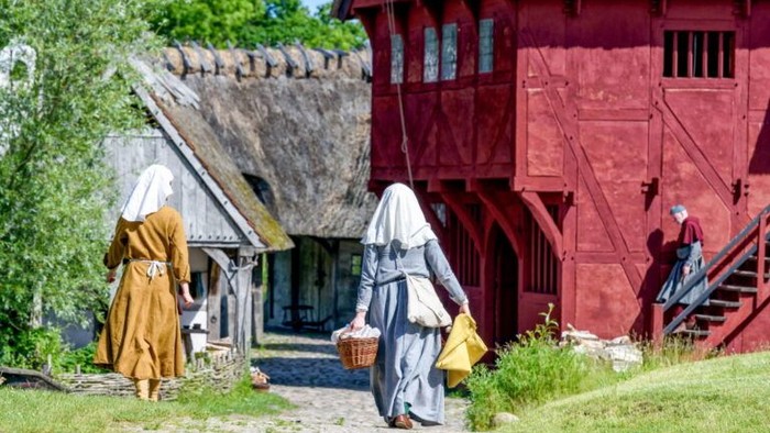 Kvinder i historiske klinger går forbi røde og grå huse.