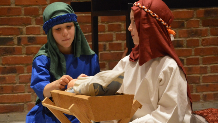 To kvinder i kostumer, den ene holder en baby i en trækrybbe.