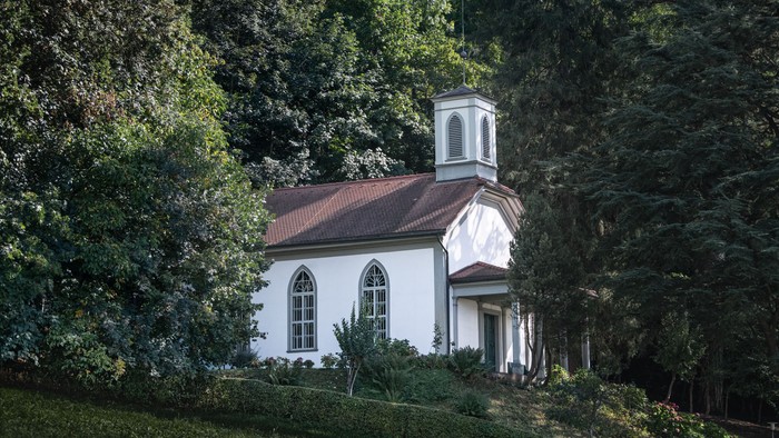 Kleine weiße Kirche mit Turm in grünem Garten.