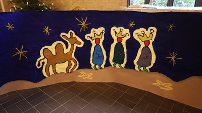 En juledekoreret scene med tre vise-mænd og en kamel foran et blåt skib.