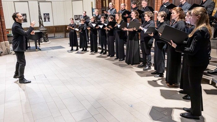 Ein Chor probt in einem prächtigen Saal unter der Leitung eines Dirigenten, gekleidet in formelle Kleidung.
