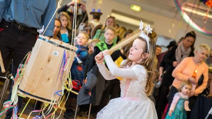 En lille pige i prinsessekostume danser ved en fest med andre børn og voksne i baggrunden