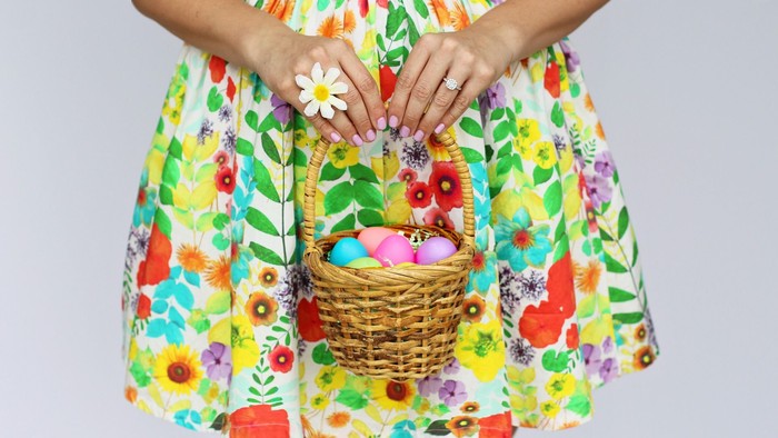 En person holder en kurv med farvet æg og en kvinde med farverig blomsterklejnet skørt.