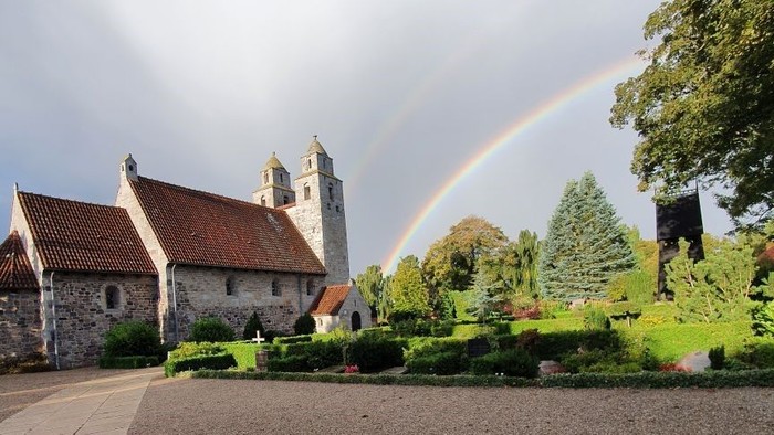 En regnbue over en gammel kirke med omgivelser.