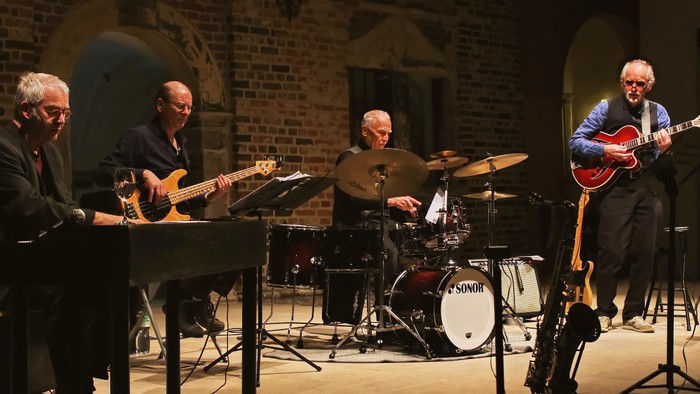 Eine Band spielt in einem Konzertsaal, vier Musiker mit Gitarren und Schlagzeug.