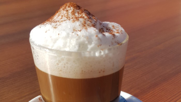 Ein Glas Kaffee mit Sahne und Zimt auf einem Teller mit Löffel