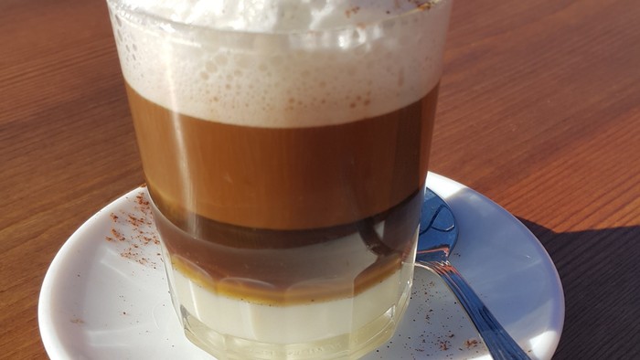 Ein Glas Kaffee mit Sahne und Zimt auf einem Teller mit Löffel