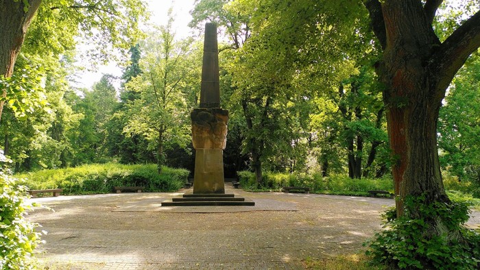 Obelisk aus Stein inmitten einer runden Freifläche umsäumt von grünen Bäumen