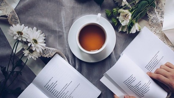Eine Person liest zwei Bücher und trinkt Tee neben Blumen.