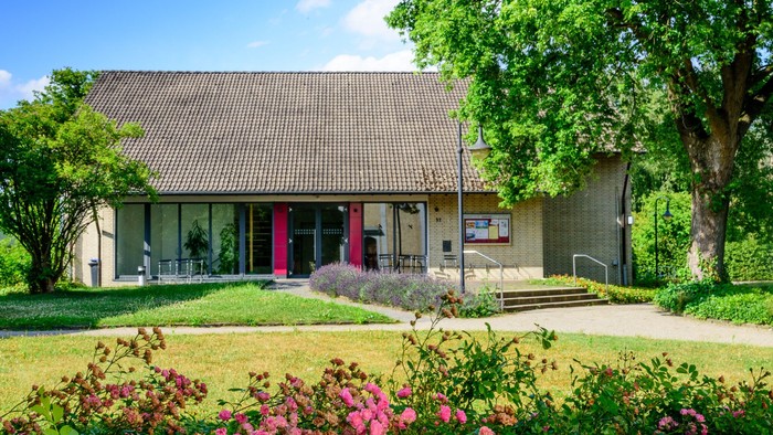 Ein modernes Haus mit großem Glasfenster und umgeben von üppigem Grün und blühenden Büschen.