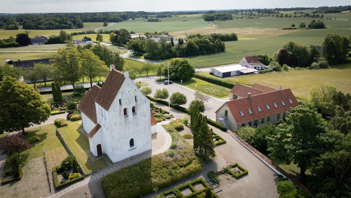 En lille landsby med en kirke og flere huse omgivet af grønne felter og træer