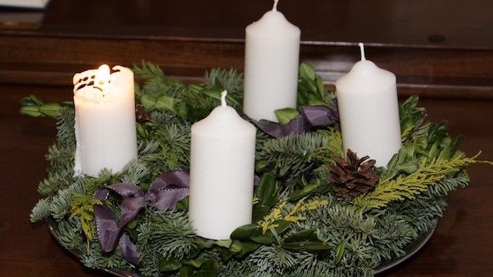En juledekorasjon med tre lysende lygter og grønne blader på en skive