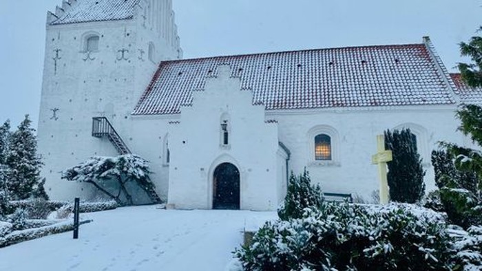 En snede hvid kirke med tårn og røde tag.