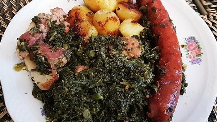 Das Bild zeigt ein Gericht mit Fleisch, Kartoffeln, Wurst und Grünkohl