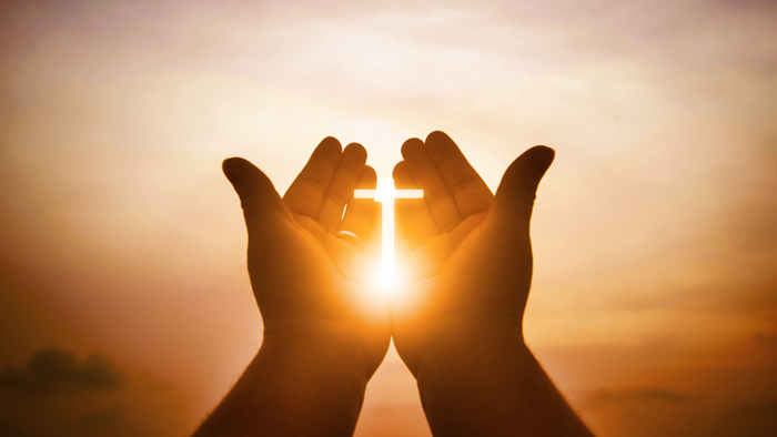 Des mains formant une croix devant le soleil couchant