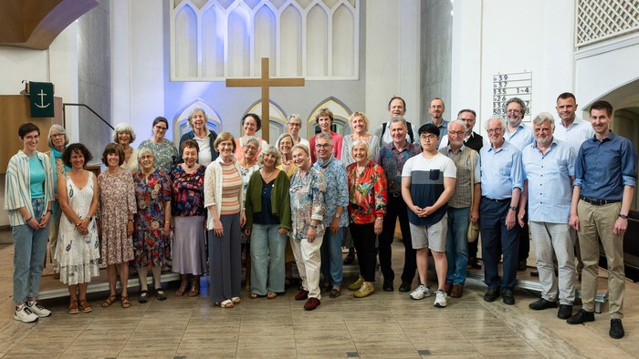 Eine vielfältige Gruppe von Menschen, die gemeinsam in einer Kirche posieren, mit einem großen Kreuz im Hintergrund.