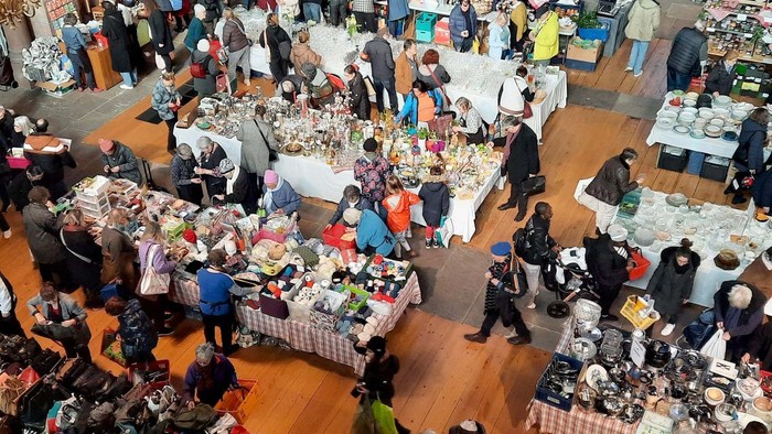 Marché animé avec divers articles en vente et nombreux acheteurs.