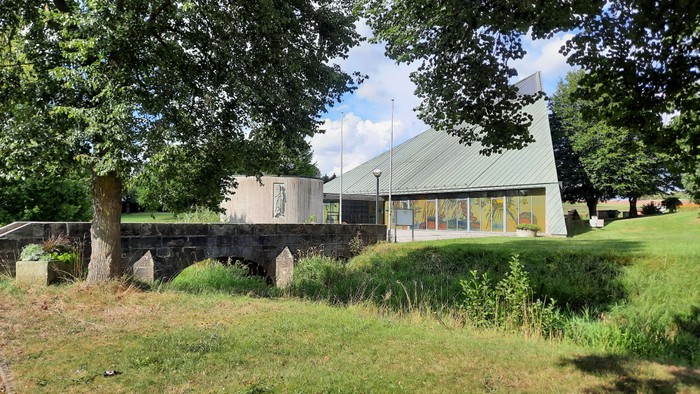 Ein modernes Haus mit grünem Dach und großen Fenstern, umgeben von Bäumen und einem gepflegten Garten.
