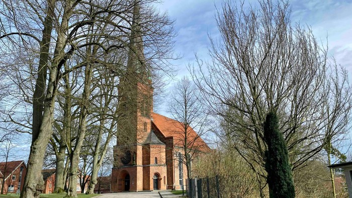 Kirchengelände mit hohem Turm und alten Bäumen