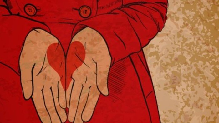 Une personne en manteau rouge tient un cœur dans ses mains.
