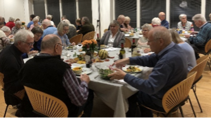 En gruppe ældre folk sidder sammen og spiser sammen i et lys og behageligt rum.