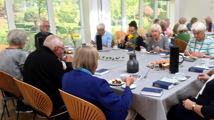 En gruppe ældre personer sidder ved et bord og spiser.