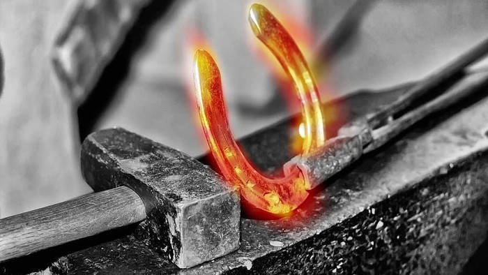 En glødende jernstang holdes i en vipp og smedes på en ammer.