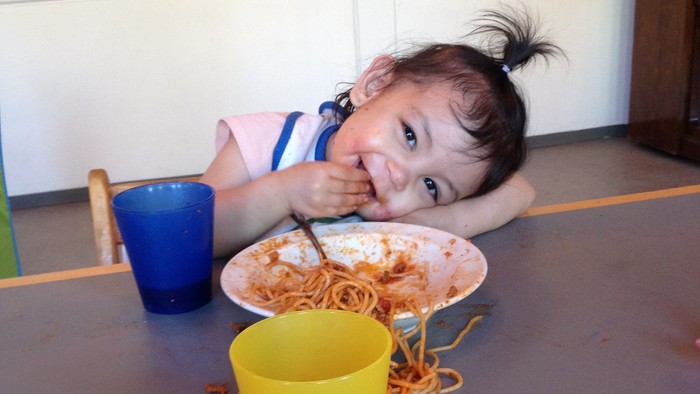 Børn spiser spaghetti på gul bord.