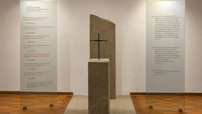 Ein feierliches Steinkreuzdenkmal mit erläuternden Texttafeln auf beiden Seiten in einem Innenraum.