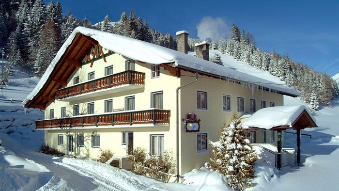 Chalet alpin charmant recouvert de neige avec des balcons en bois et un décor montagneux pittoresque en arrière-plan.