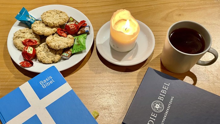 Gemütliches Frühstücksarrangement mit Keksen, Kaffee, Kerzen und Bibeln auf einem Holztisch.