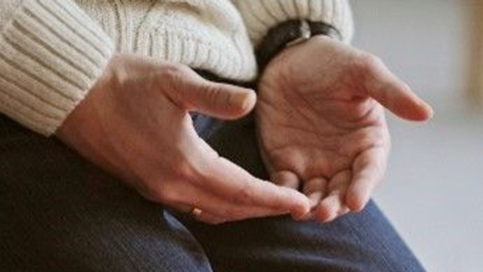 Person sitzt mit verschränkten Händen vor einer brennenden Kerze