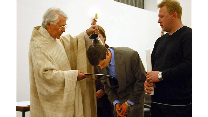 Ein älterer Mann zeigt zwei jüngeren Männern etwas an einem Tisch.