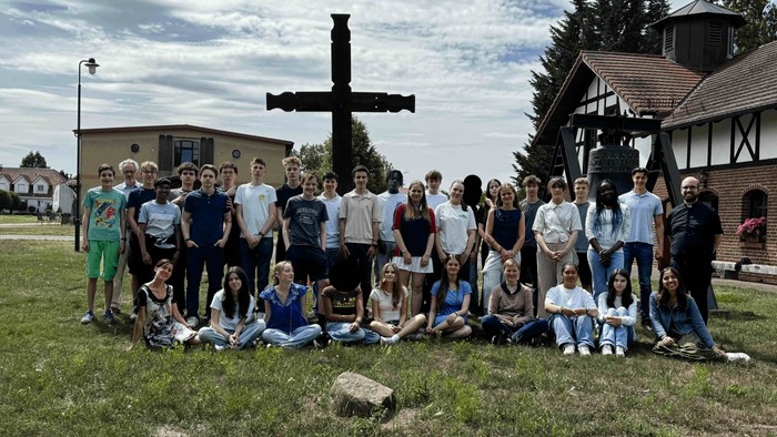 Eine Gruppe von Menschen posiert vor einem großen Kreuz auf einem grasbewachsenen Bereich.