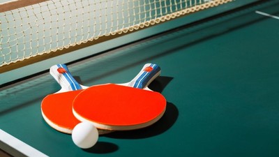 Zwei rote Tischtennisschläger und Bälle auf einem grünen Tischtennistisch.