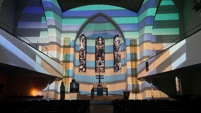 Die Kirche ist farbig beleuchtet, der Altar ist prominent in der Mitte.