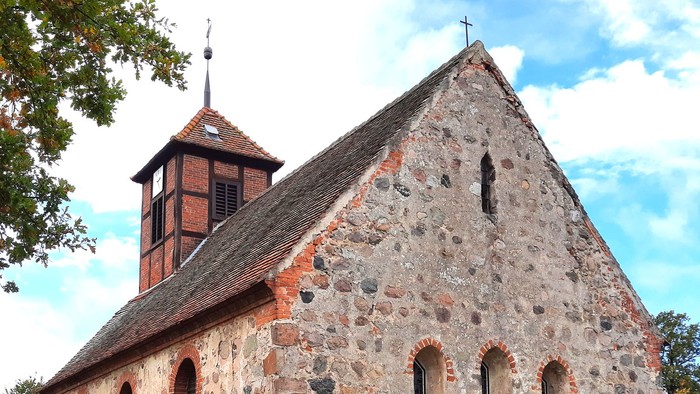 Steinige Kirche mit Turm auf grünem Hügel unter blauem Himmel