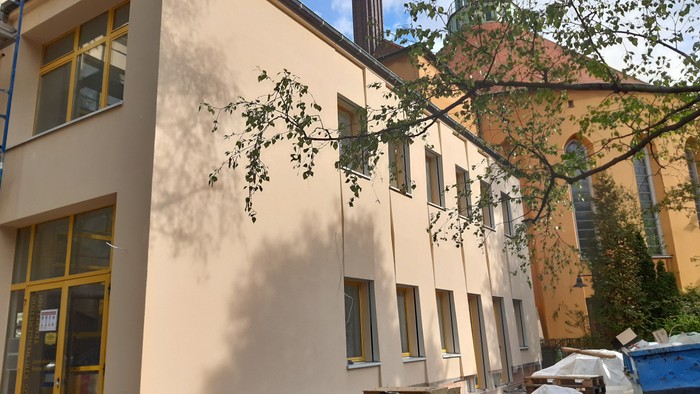Das Bild zeigt ein beigefarbenes Gebäude mit großen Fenstern und einem Baum davor.